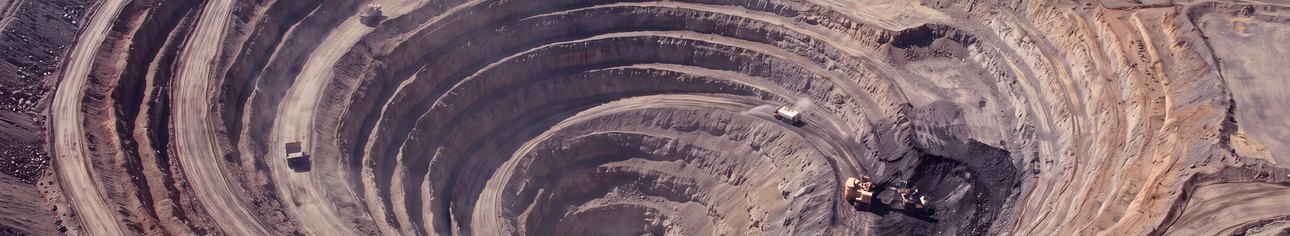 An open-pit mine seen from above, haul trucks on the benches