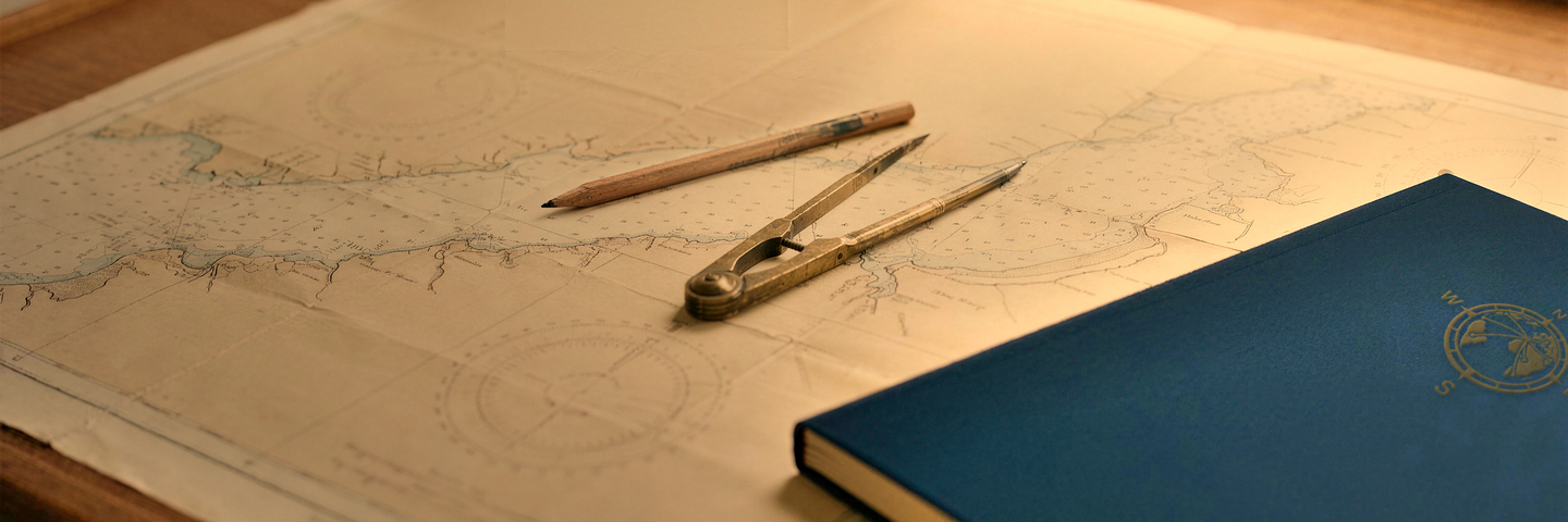 A nautical chart spread on a table with dividers, a pencil and a navy notebook