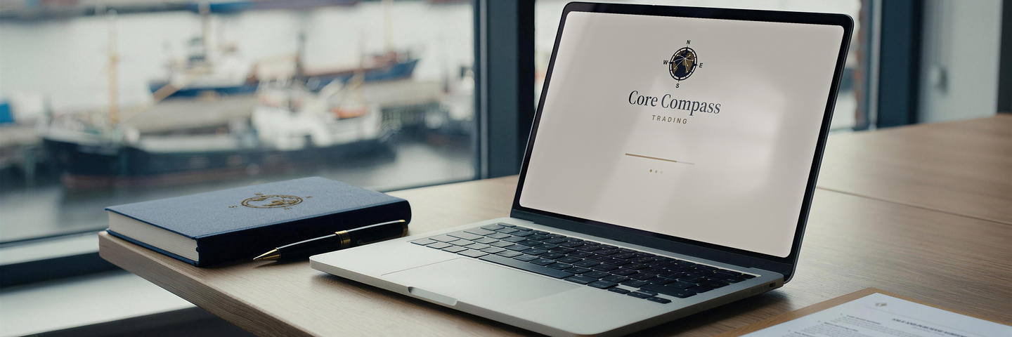 A laptop on a desk by a harbour window, a navy notebook beside it